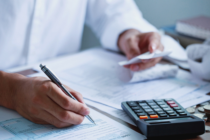 Close-up of a person reviewing financial documents at a desk, holding receipts and using a calculator. | Kraft Miles, A Law Corporation